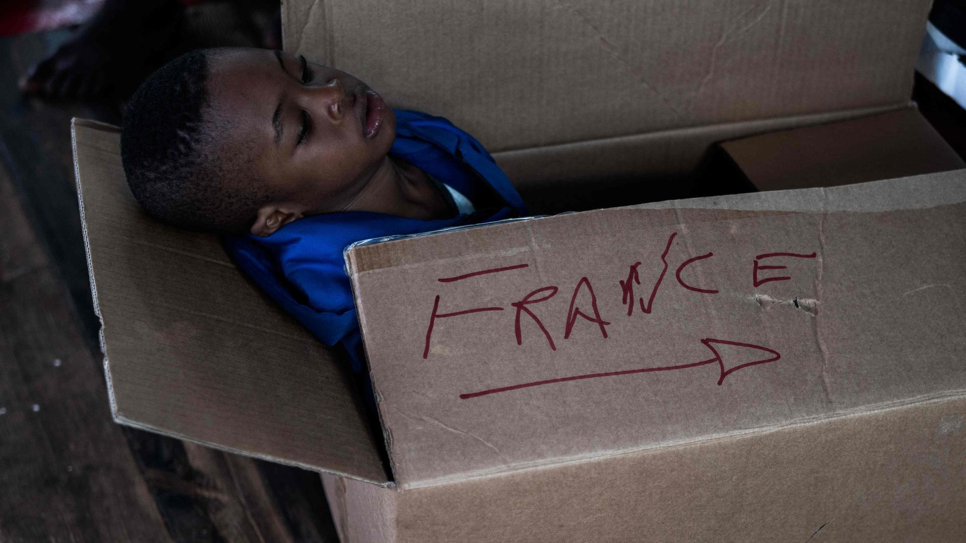 A migrant child sits in a cardboard box with the inscription "France" aboard the Ocean Viking rescue ship on November 10, 2022 in the Tyrrhenian Sea between Italy and Corsica island. - France said on November 10, 2022 that it would allow a rescue ship carrying more than 200 migrants to dock on its southern coast and disembark its passengers, harshly criticising Italy for failing to take them in. (Photo by Vincenzo Circosta / AFP)