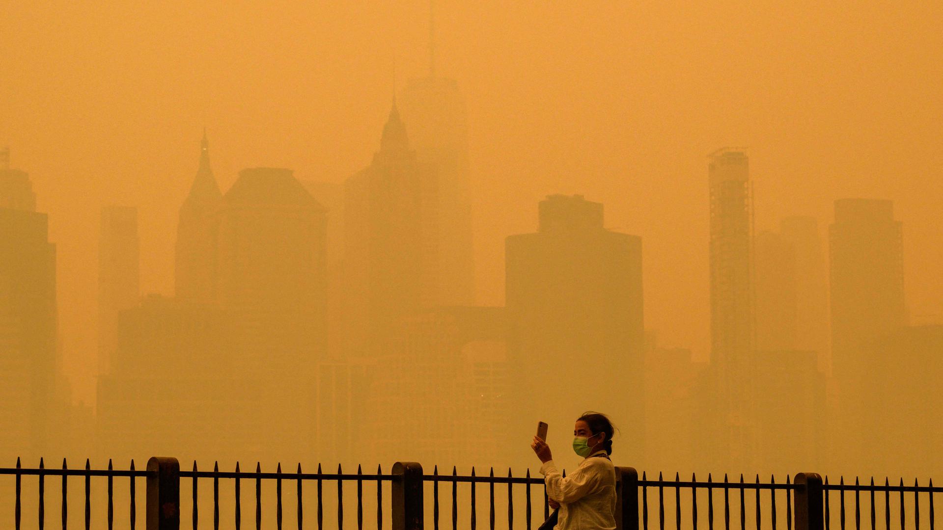 TOPSHOT - A person wearing a face mask takes photos of the skyline as smoke from wildfires in Canada cause hazy conditions in New York City on June 7, 2023. An orange-tinged smog caused by Canada's wildfires shrouded New York on Wednesday, obscuring its famous skyscrapers and causing residents to don face masks, as cities along the US East Coast issued air quality alerts. (Photo by ANGELA WEISS / AFP)