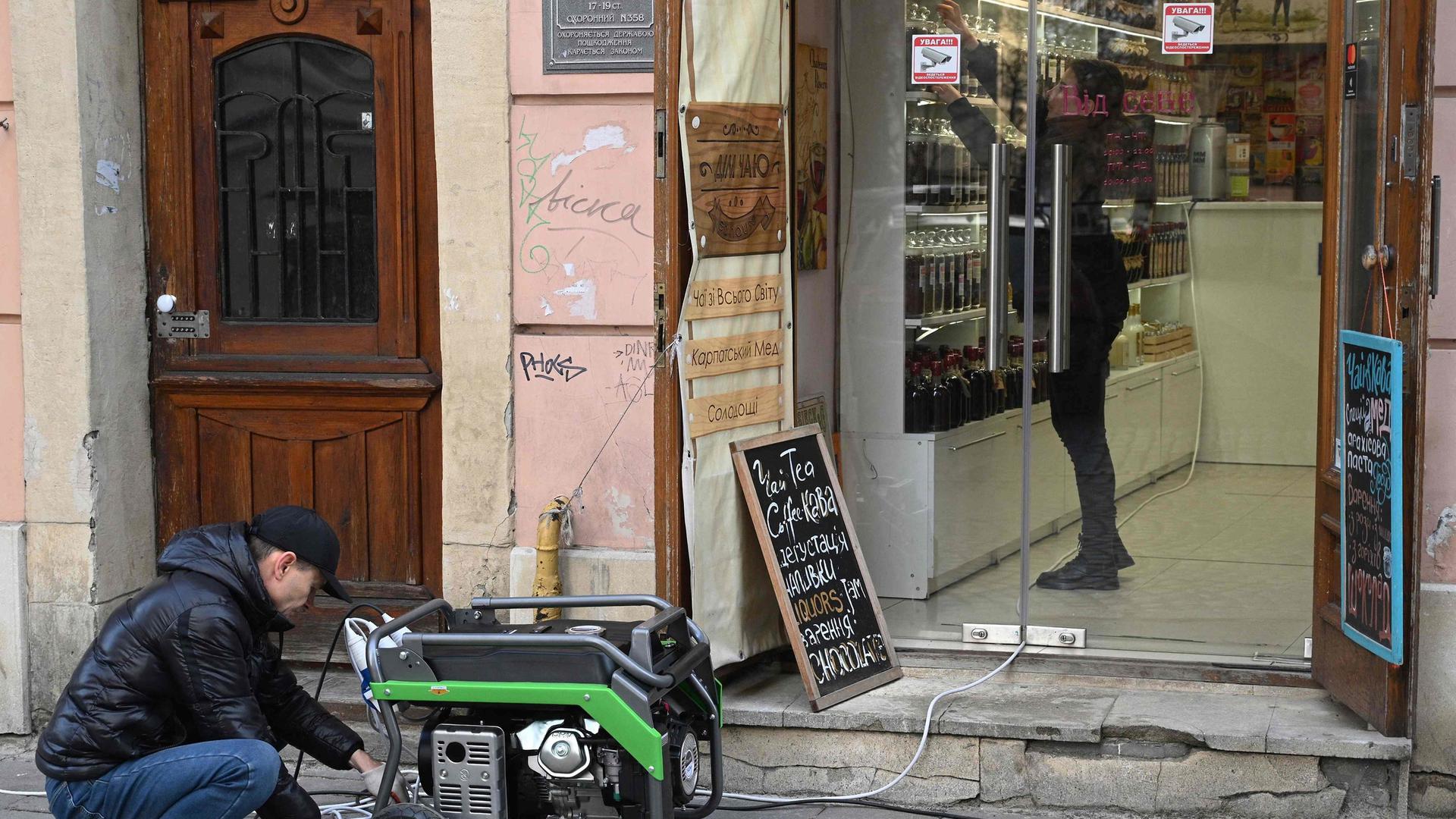 Um homem manuseia um gerador à porta de uma loja durante um apagão causado pelos mísseis russos, em Lviv, esta quinta-feira 