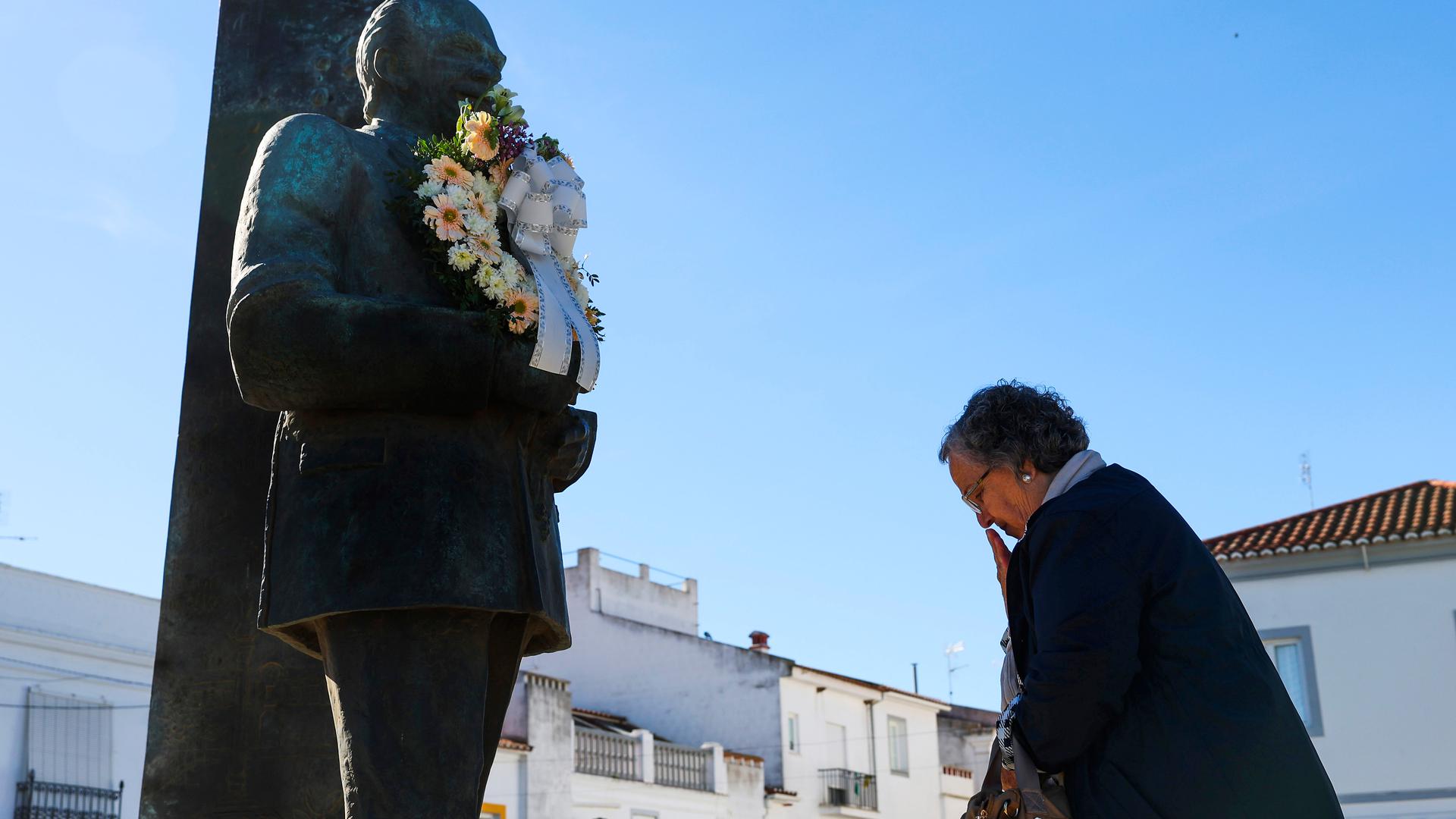Uma mulher reza junto à estátua do empresário Rui Nabeiro, momentos antes da passagem cortejo fúnebre, na rotunda de entrada em Campo Maior, 20 de março de 2023. O empresário Rui Nabeiro, fundador do Grupo Nabeiro - Delta Cafés, morreu no domingo, aos 91 anos, vítima de doença, no Hospital da Luz, em Lisboa. NUNO VEIGA/LUSA
