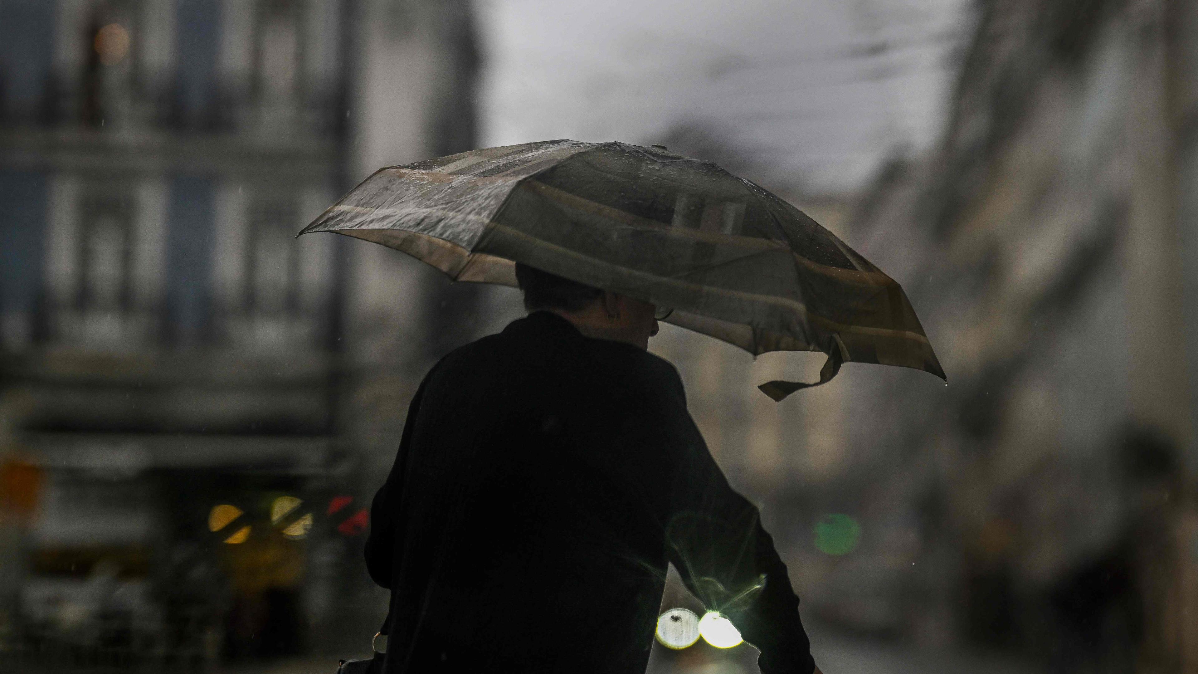 A woman takes shelter under an umbrella during a heavy rain caused by storm Aline in Lisbon, on October 19, 2023. Portugal was hit by violent winds and heavy rain which caused flooding and falling trees, especially in the regions of Lisbon and Porto (north), civil protection said. (Photo by Patricia DE MELO MOREIRA / AFP)