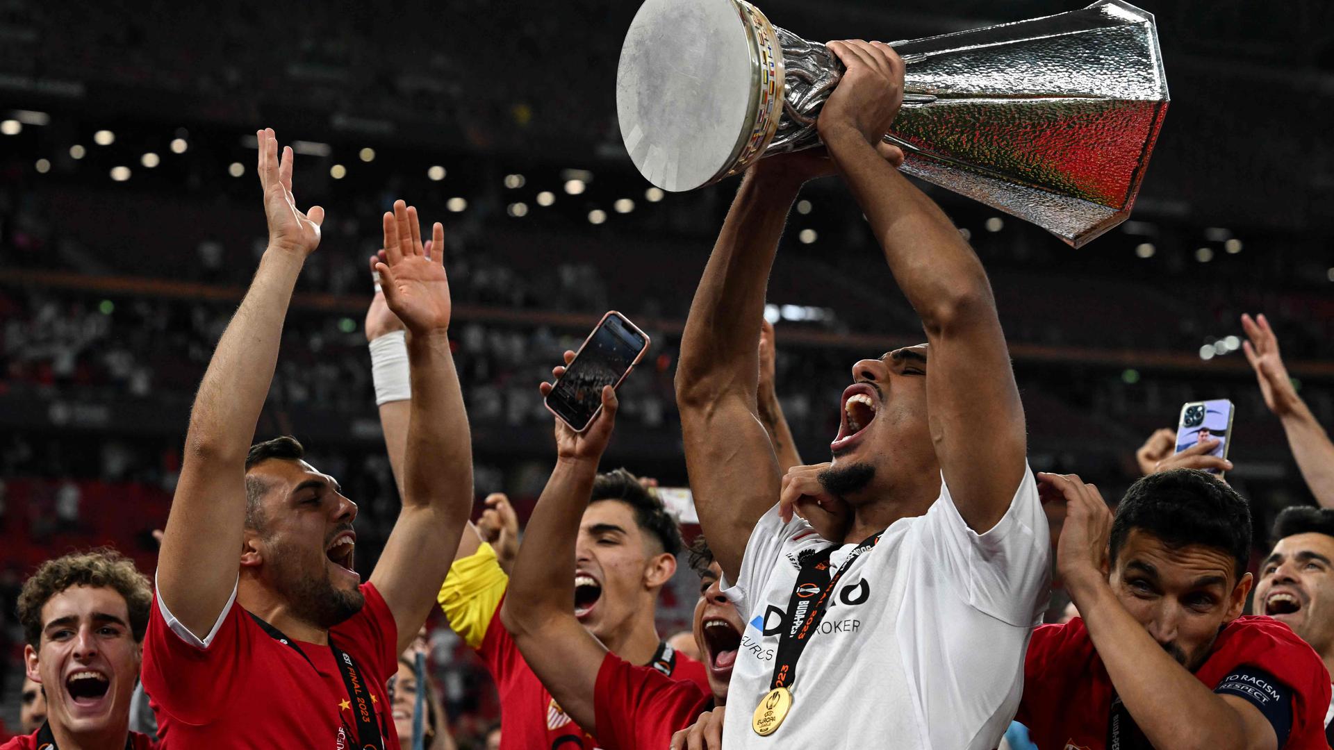 TOPSHOT - Sevilla's French defender Loic Bade (R) carries the trophy as he celebrates with the fans after winning the UEFA Europa League final football match between Sevilla FC and AS Roma at the Puskas Arena in Budapest on May 31, 2023. (Photo by VLADIMIR SIMICEK / AFP)