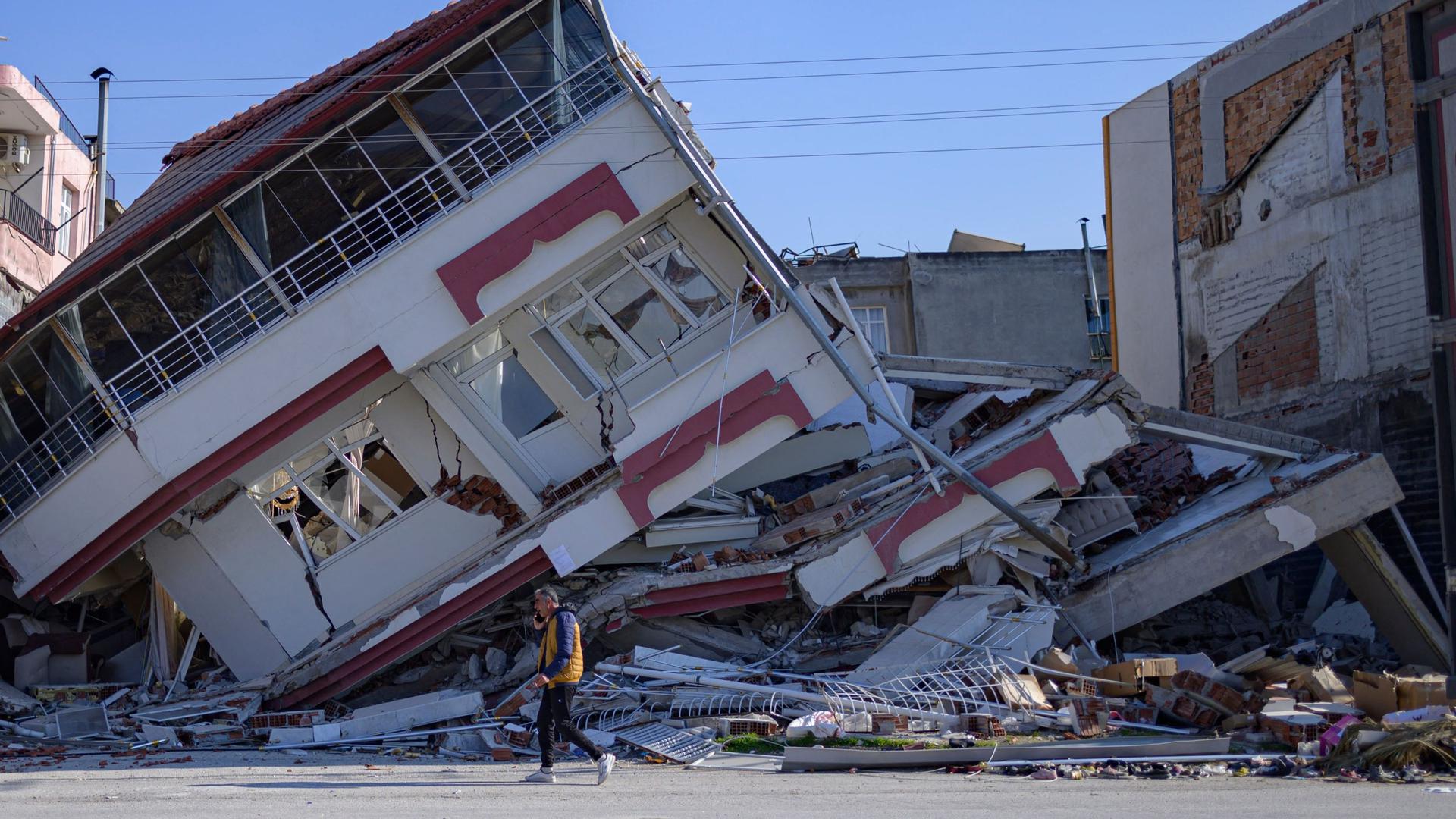 Um homem caminha em frente a um edifício destruído em Samandag, a sul de Hatay, Turquia.