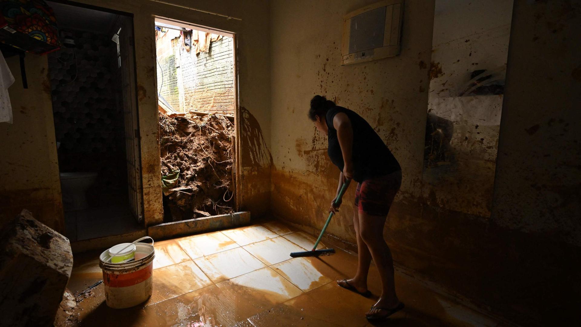 Uma mulher limpa o chão da casa inundado pelas chuvas torrenciais, no distrito de Juquehy, São Sebastião.