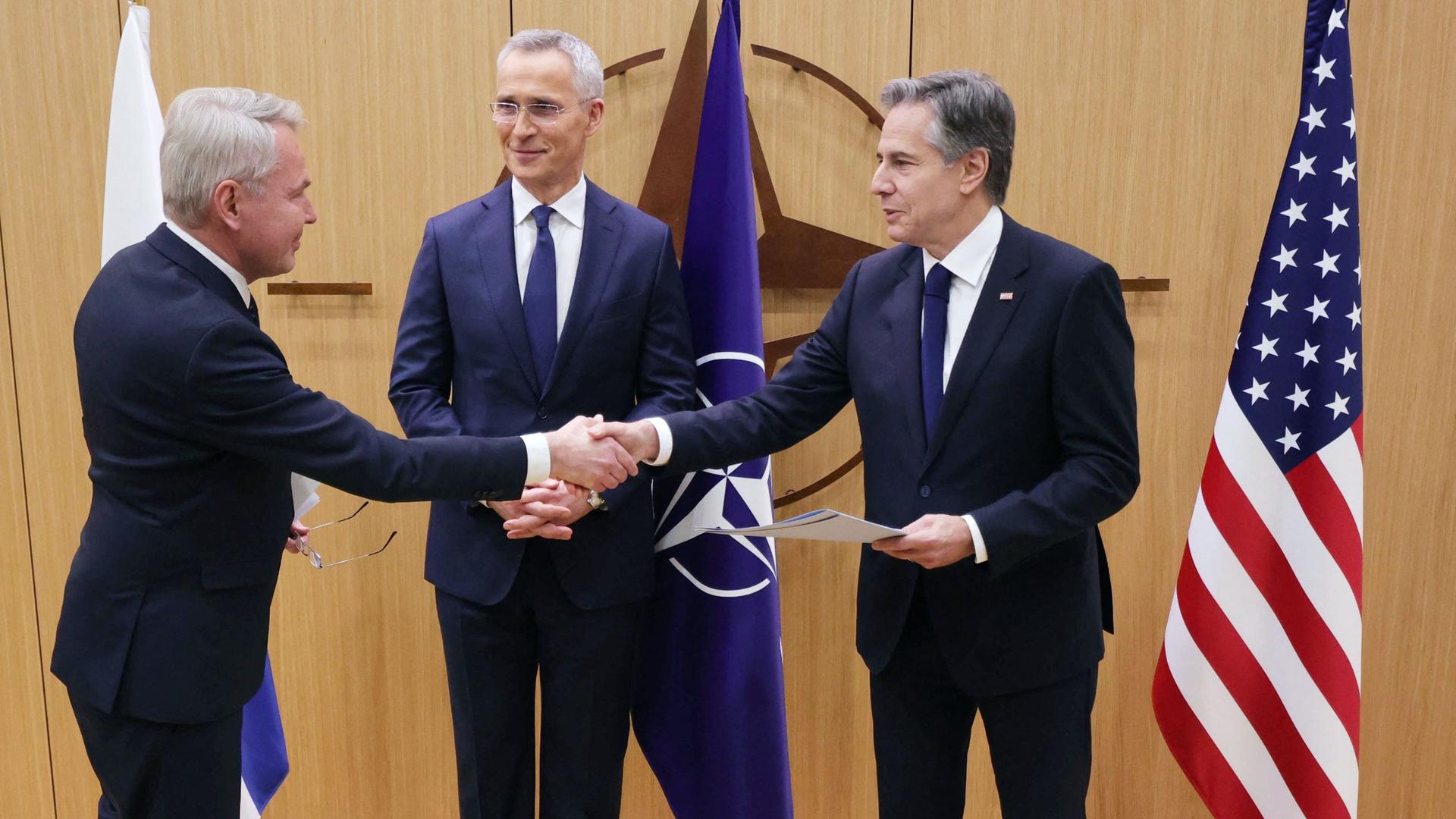 Ministro finlandês dos Negócios Estrangeiros, Pekka Haavisto, aperta a mão ao Secretário de Estado norte-americano Antony Blinken, acompanhado pelo Secretário-Geral da NATO, Jens Stoltenberg