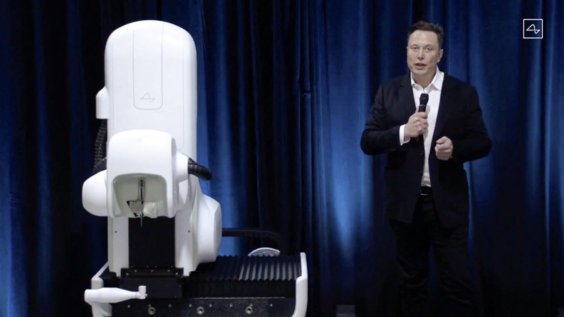 Elon Musk ao lado do robô cirúrgico durante a apresentação da Neuralink. 
