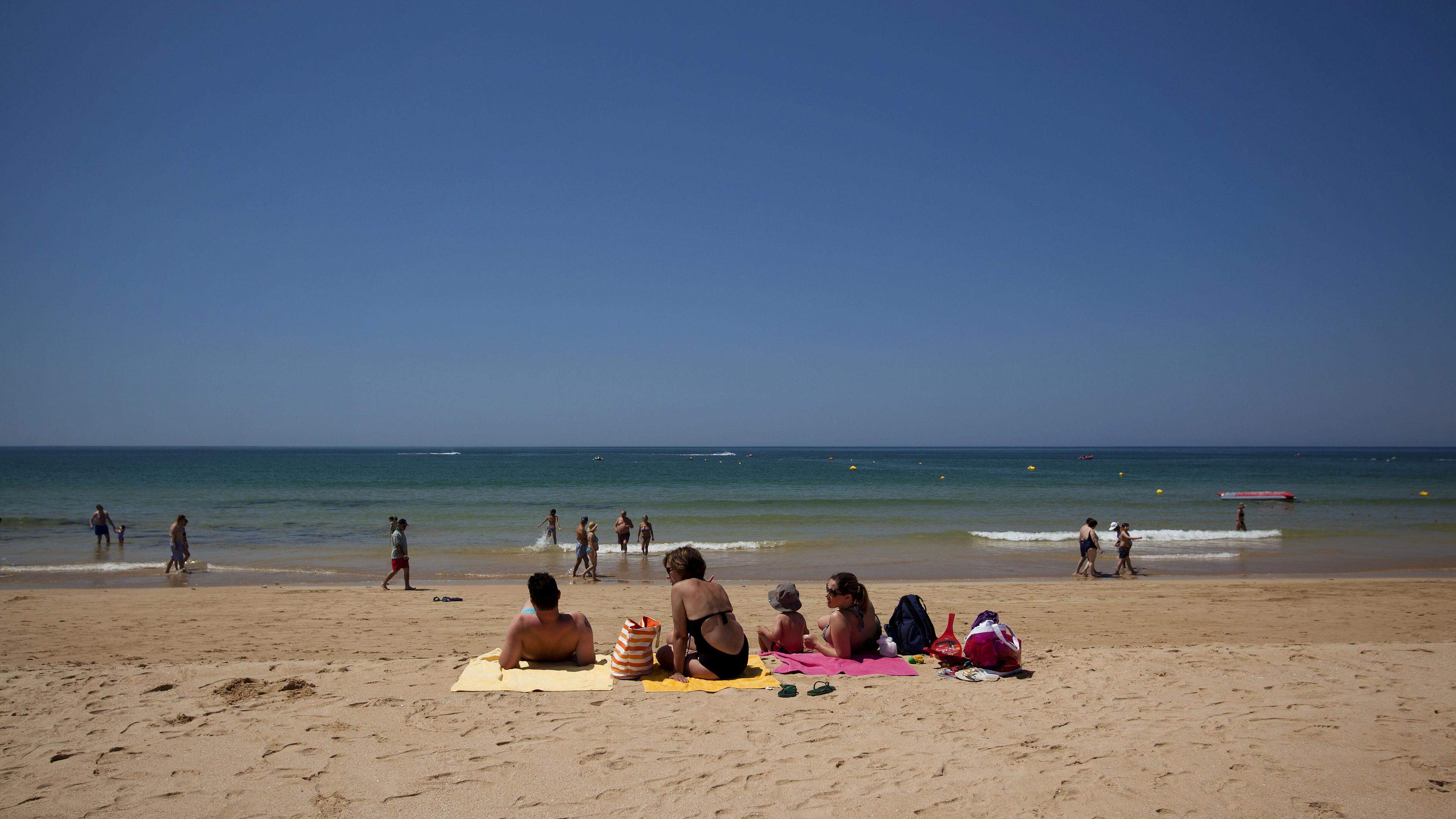 Populares descansam deitados junto à água na praia, em Portimão.