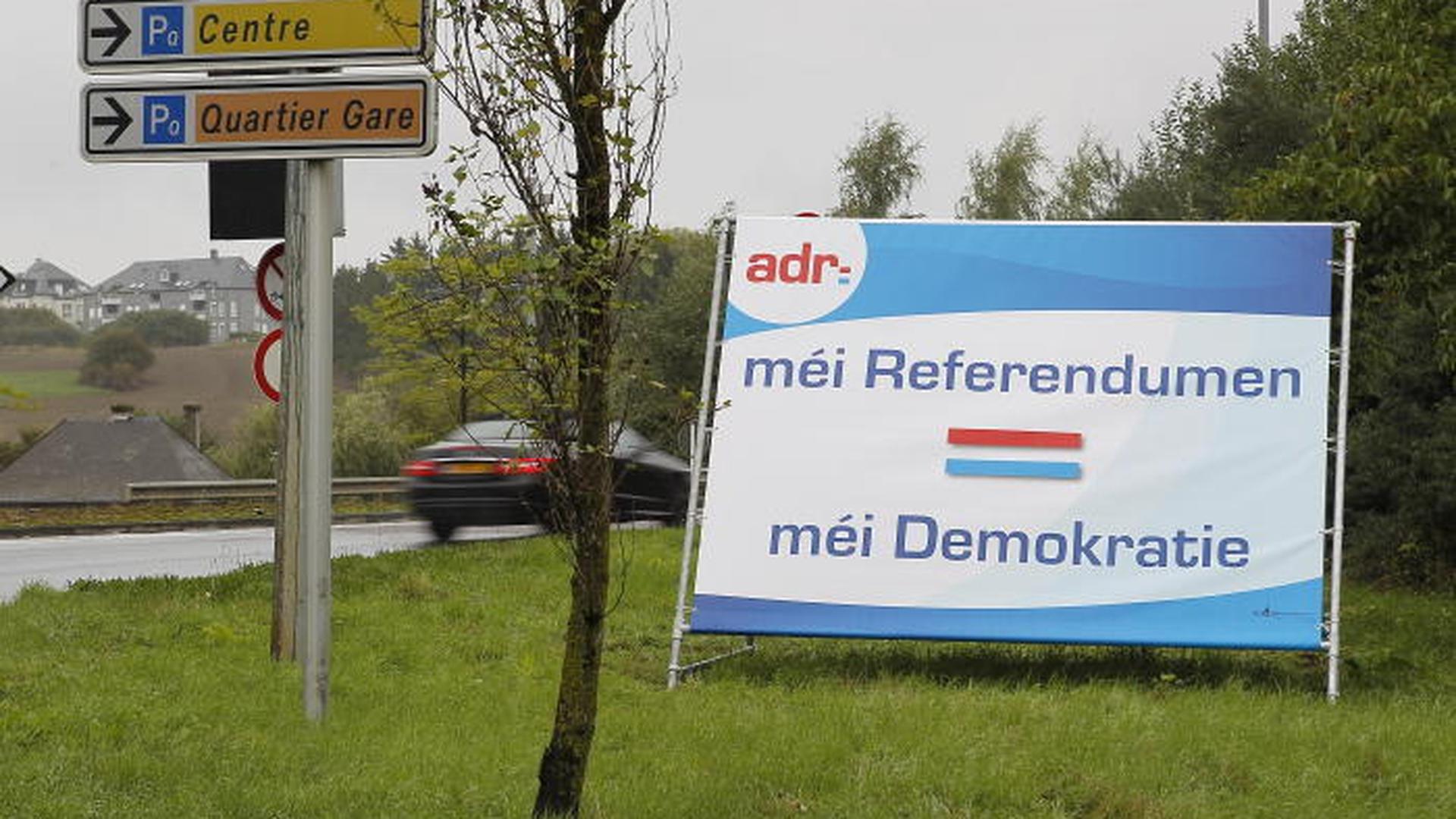 A campanha do ADR, o partido mais à direita no espectro político luxemburguês, aposta em afirmações populistas, reforçando a imagem de partido nacionalista com uma bandeira luxemburguesa. A bandeira, no centro dos "outdoors", simboliza o sinal matemático "igual" (=). Este cartaz diz: "Mais referendos = mais democracia".