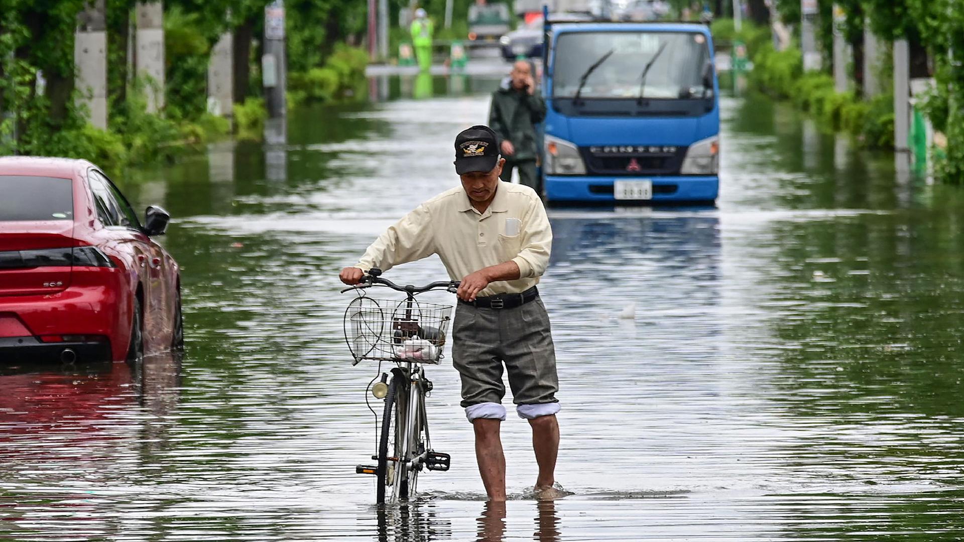 A man pushes a bicycle down a road closed due to flooding at Koshigaya, Saitama Prefecture on June 3, 2023, after heavy rains caused by passing Tropical Storm Mawar hit much of the country the day before. Heavy rain across parts of Japan has killed one person, left two missing and injured dozens more, authorities said on June 2, with thousands of residents issued evacuation warnings. (Photo by JIJI Press / AFP) / Japan OUT