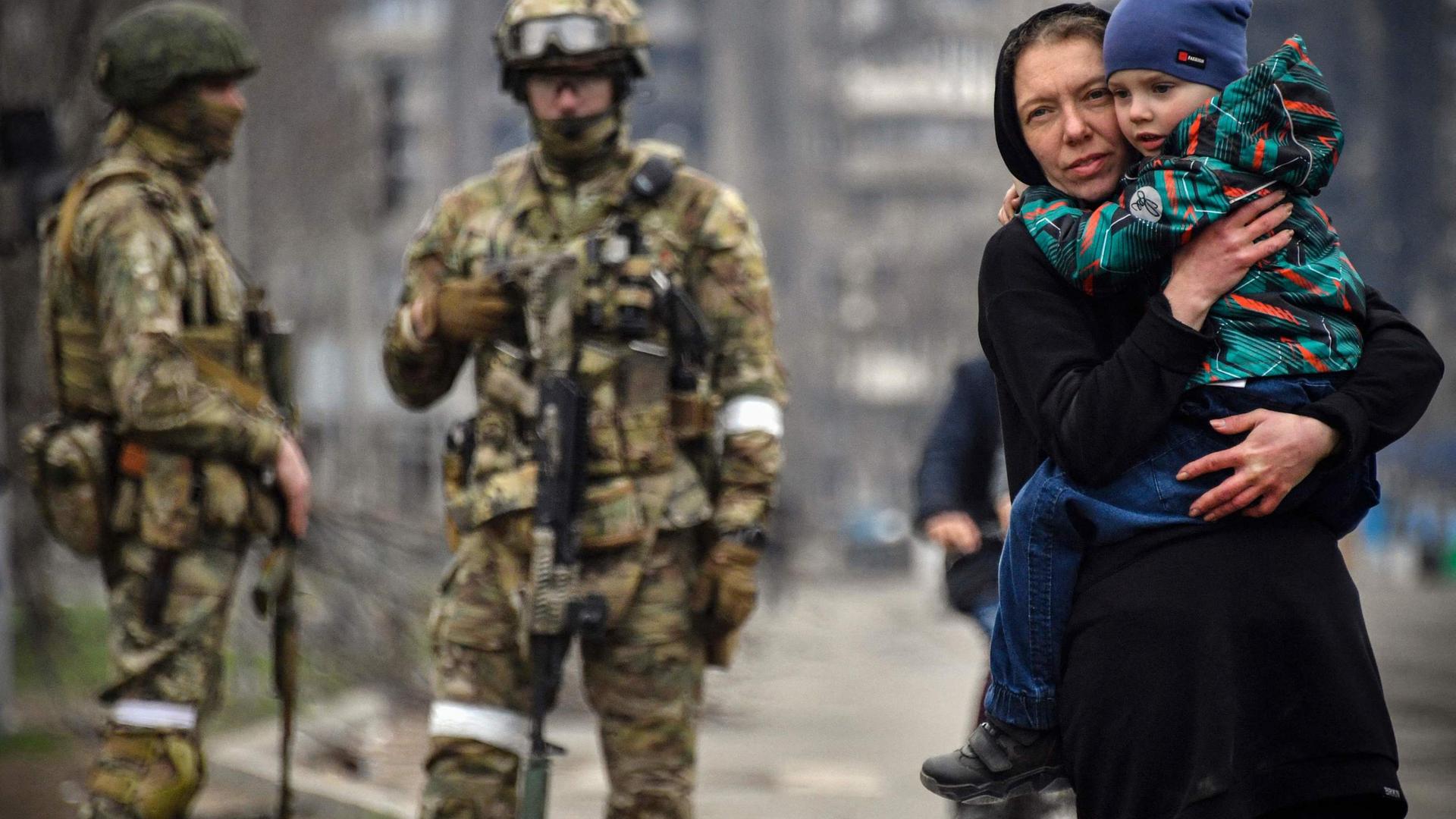 Imagem de uma residente de Mariupol caminhando com o filho sob o olhar das tropas russas.