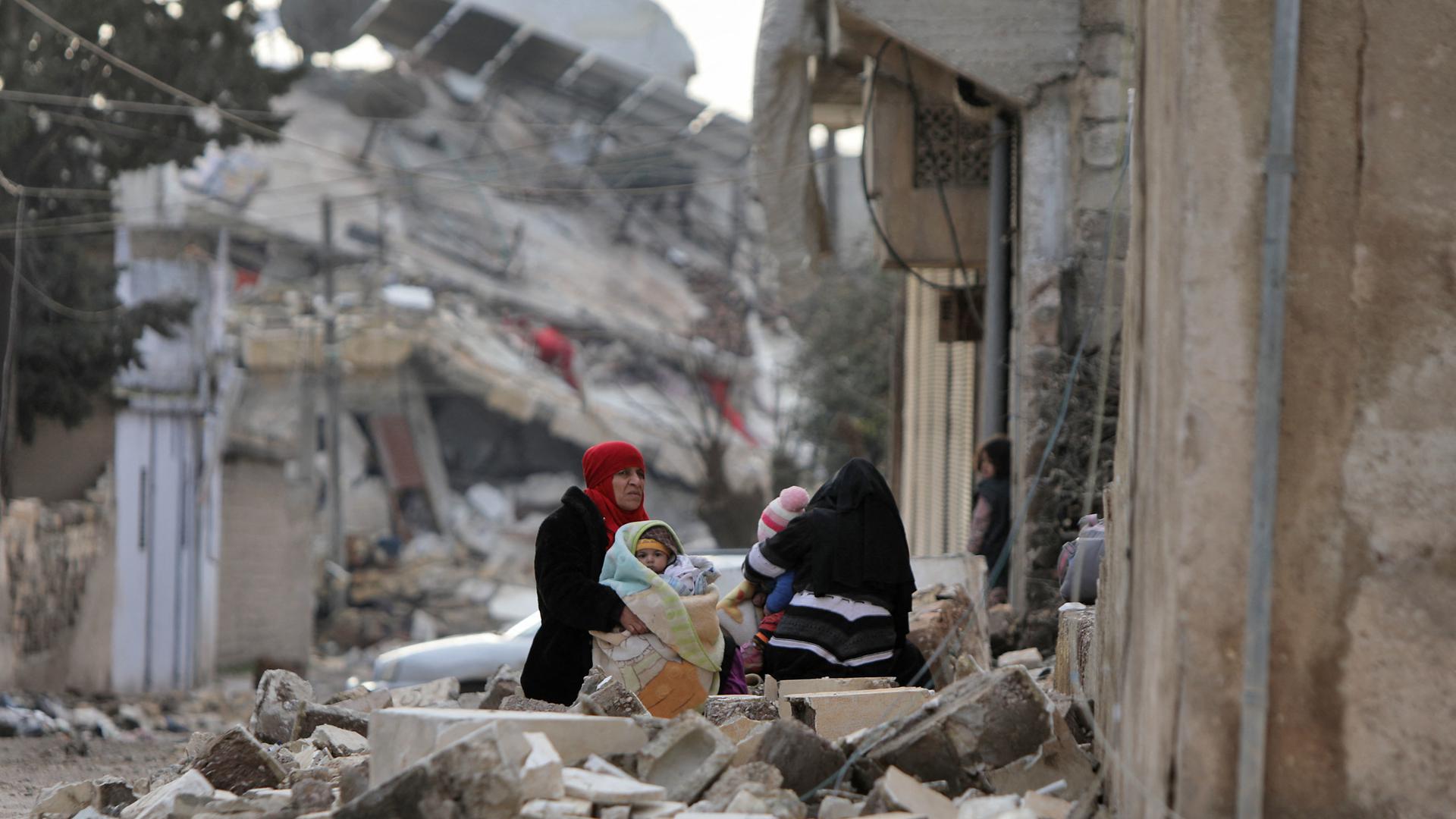 Mulheres e crianças sírias no exterior de edifícios desmoronados na cidade de Jandairis, Aleppo