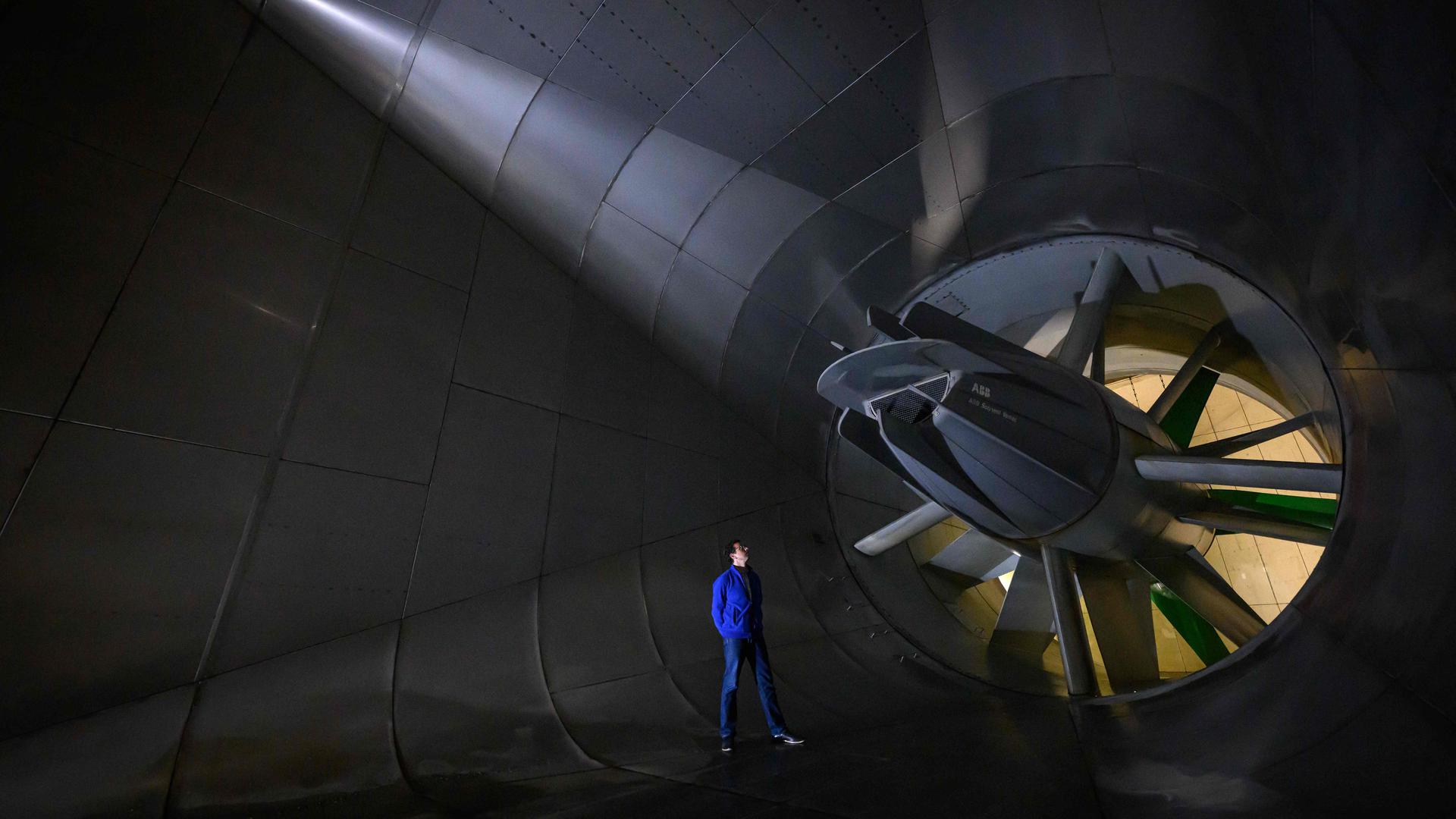 TOPSHOT - An employee of the CSTB (Centre scientifique et technique du batiment, or Scientific and Technical Centre for Building) stands next to a giant fan of the Jules Verne Climatic Wind Tunnel, a research facility used to study and analyse the building and construction elements under the extreme climatic conditions, in Nantes, western France, on May 9, 2023. (Photo by LOIC VENANCE / AFP)